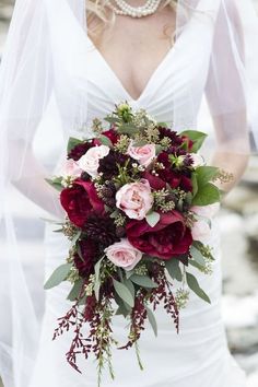 a bride holding a bouquet of red and pink flowers