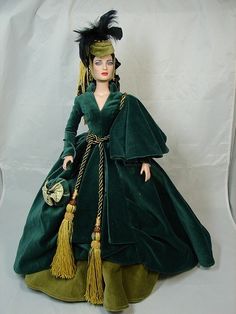 a doll is dressed in green and wearing a long dress with tassels on it