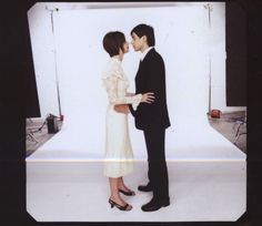 a man and woman standing next to each other in front of a white backdrop with lights