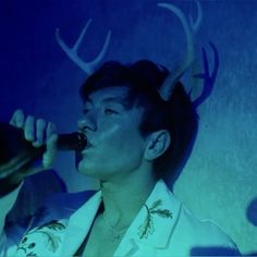 a man with horns on his head is singing into a microphone in front of a blue background