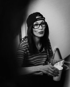 black and white photograph of a woman in glasses holding a coffee cup while sitting on a chair