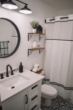 a white toilet sitting next to a bathroom sink under a mirror and a black and white shower curtain