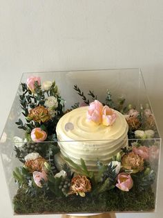 a cake with frosting and flowers in a glass box on top of a table