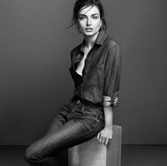 a woman sitting on top of a wooden block wearing jeans and a denim shirt, posing for a black and white photo