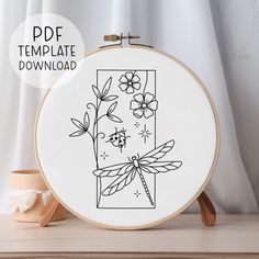 a cross stitch pattern with flowers and a dragonfly on it, in front of a white background