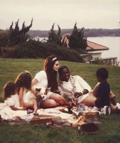 a group of people sitting on top of a lush green field next to a lake