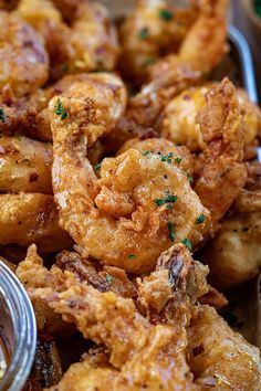 some fried food is sitting in a bowl with dipping sauce on the side and garnished with parsley