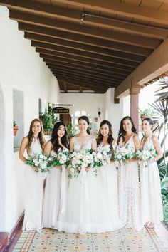 a group of women standing next to each other in front of a building holding bouquets