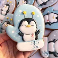 a hand holding a cookie shaped like a penguin with stars on its chest and penguins in the background