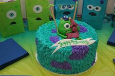 a green and purple cake sitting on top of a table next to blue bags filled with candy