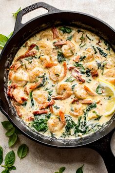 a skillet filled with shrimp, spinach and cheese on top of a table