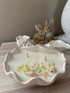 two little bunnies sitting on top of a table next to a white bowl filled with food