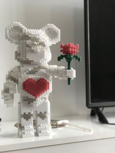 a lego bear holding a red rose on top of a white shelf next to a computer monitor