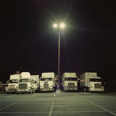 several white trucks parked in a parking lot under a street light at night with the lights on