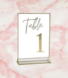 a table number is placed on a marbled surface with gold trim and a pink background