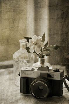 an old camera sitting on top of a table next to a vase filled with flowers