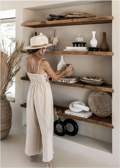 a woman standing in front of shelves holding a jug and looking at items on the shelf