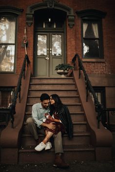 a man and woman sitting on the steps in front of a brick building holding each other