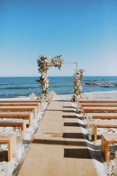 an outdoor ceremony set up with wooden benches and flowers on the aisle leading to the beach