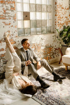 a man and woman sitting on the floor in front of a brick wall, with their feet up