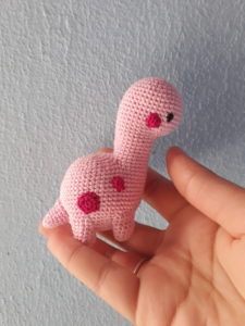 a tiny pink crocheted animal sitting on top of a persons hand in front of a white wall