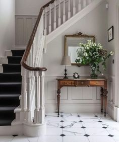 a white staircase with black and white tile flooring next to a wooden console table