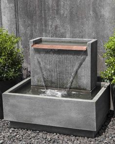 an outdoor fountain with water coming out of it and some plants in the back ground