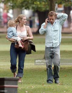 a man and woman walking in the park with a baby on their lap, talking on a cell phone