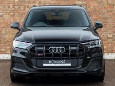 the front end of a black car parked in front of a brick wall and door