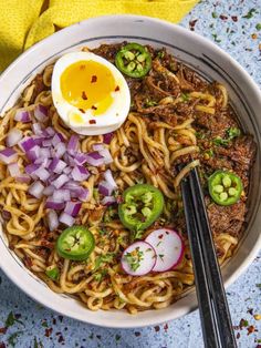 a bowl filled with noodles, meat and vegetables next to chopsticks on a table