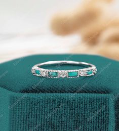 an emerald and diamond ring sits on top of a green velvet box, with a white background