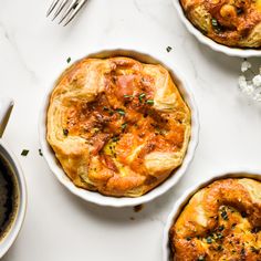 three different types of food in white bowls on a table with utensils and silverware