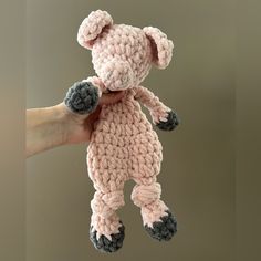 a hand holding a pink crocheted teddy bear in it's right arm