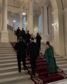 several people are walking up and down the stairs in an elegant building with red carpet