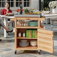 a woman sitting at a kitchen island with plates and glasses on it, in front of an outdoor dining area