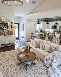 a living room filled with furniture and a chandelier hanging from the ceiling in front of a kitchen