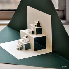 an origami house on top of a green table next to a large window