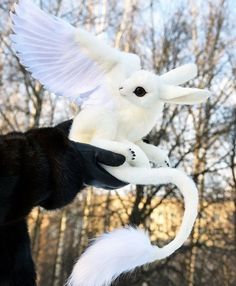 a white stuffed animal flying through the air with trees in the back ground behind it