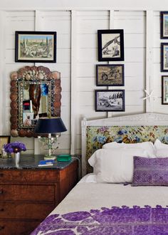 there is a bed with purple and white pillows on it in the room that has many framed pictures on the wall