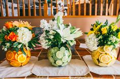 three vases filled with flowers and fruit sitting on top of a table next to each other