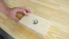 a person holding a piece of wood on top of a wooden table with a hole in it