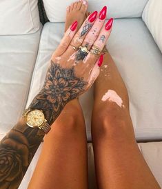 a woman with red nails and tattoos on her legs is sitting on a white couch