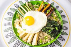 a green plate topped with rice and vegetables next to an egg on top of it