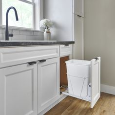 a white trash can is open in the middle of a kitchen with wood floors and cabinets