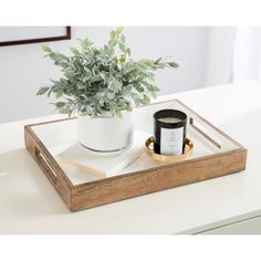 a wooden tray holding a candle and a potted plant on top of a white table