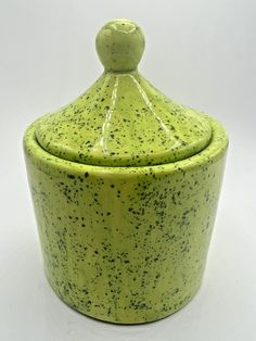 a green ceramic container with a lid and sprinkles on the top, sitting on a white surface