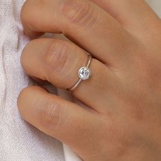 a woman's hand with a diamond ring on her left hand and a white towel in the background