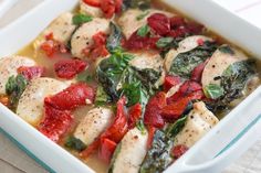 a white casserole dish filled with chicken, tomatoes and spinach in broth