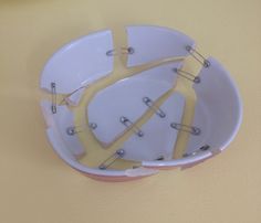 a yellow and white bowl with metal pins sticking out of the side on a wall