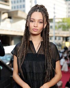 a woman with long braids standing in front of a car on the red carpet